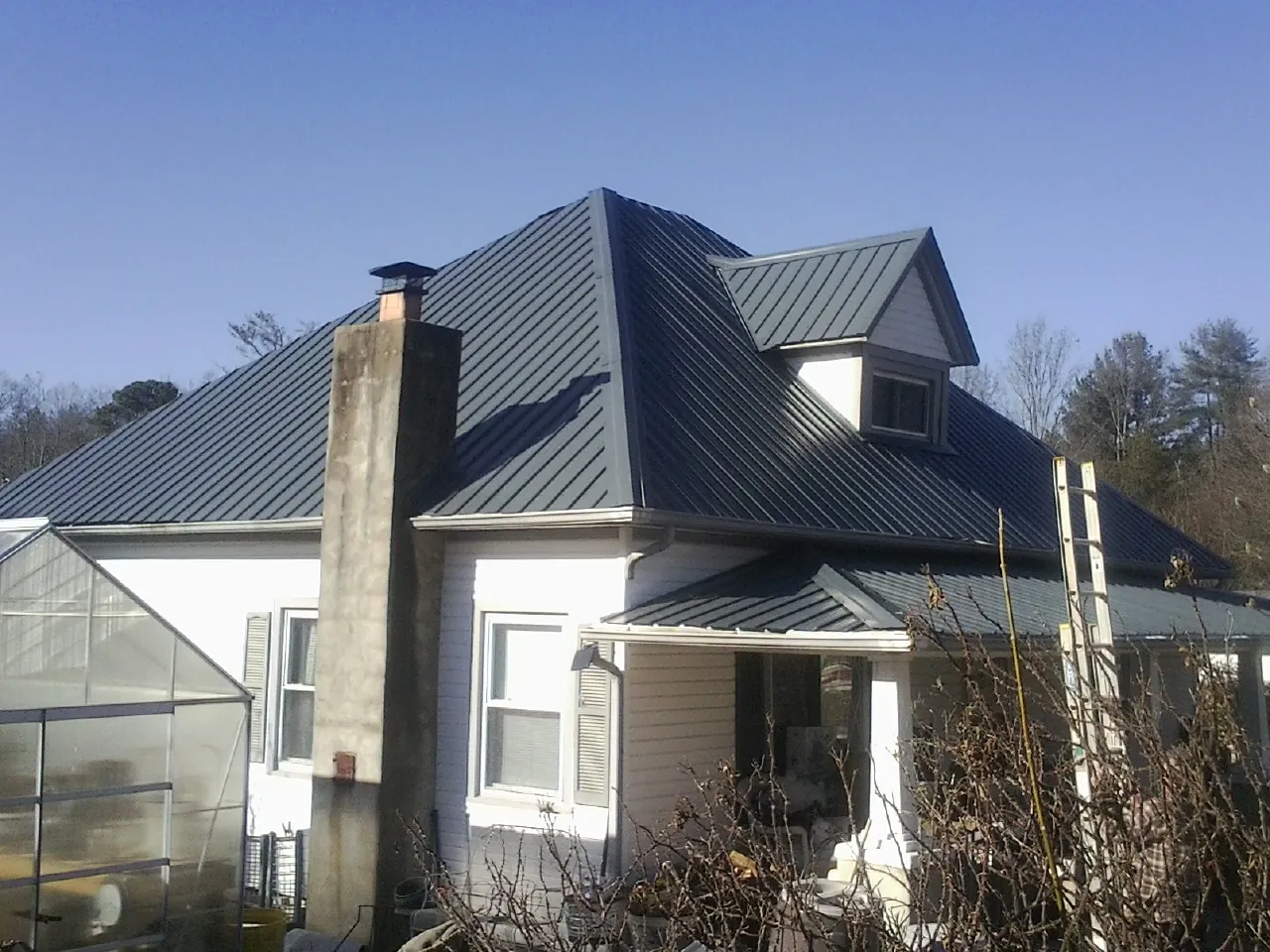 Dark blue standing seam metal roof on a white farmhouse with dormer — Slate & Tile Roof Repair by Roofing Brothers in Berthoud