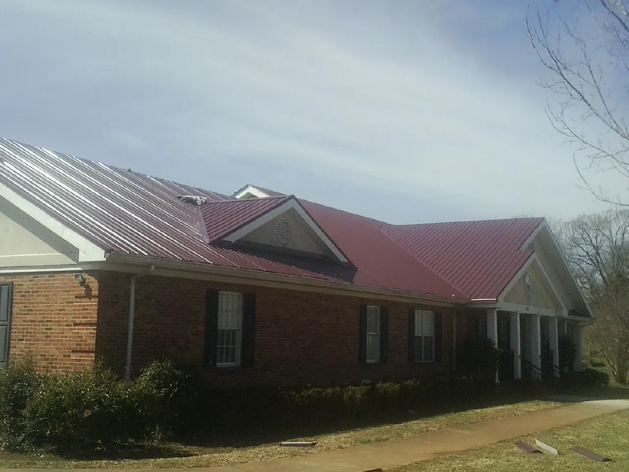 Red metal roof with gabled entries on a long brick building, from a Hail Damage Roof Repair job in Berthoud