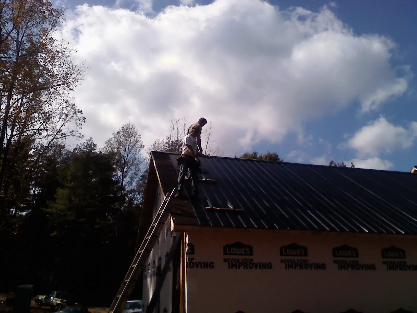 Roofer fastening dark metal panels high against a cloudy sky, from a Roof Inspection job in Berthoud