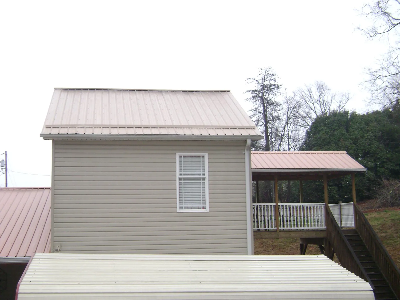 Tan metal roofs on a two story addition and attached porch, from a Roof Replacement job in Berthoud