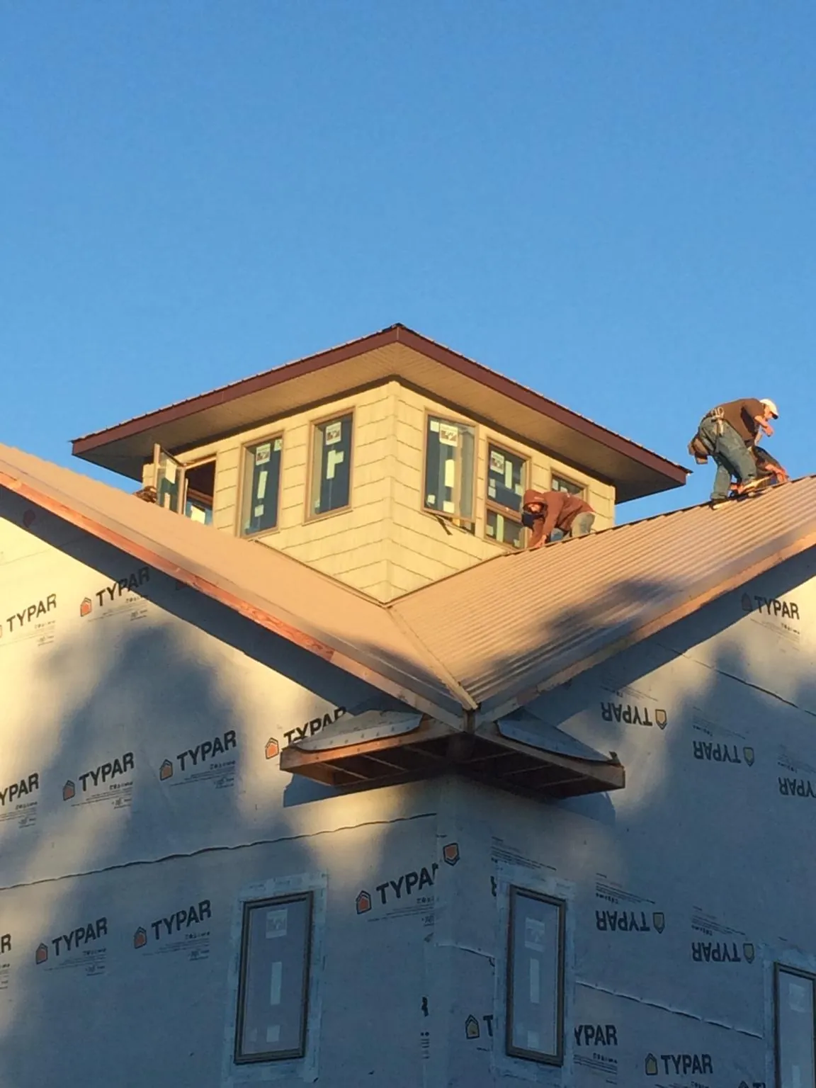 Roofers working around a rooftop cupola on a new metal roof at sunset — Roof Waterproofing in Berthoud by Roofing Brothers